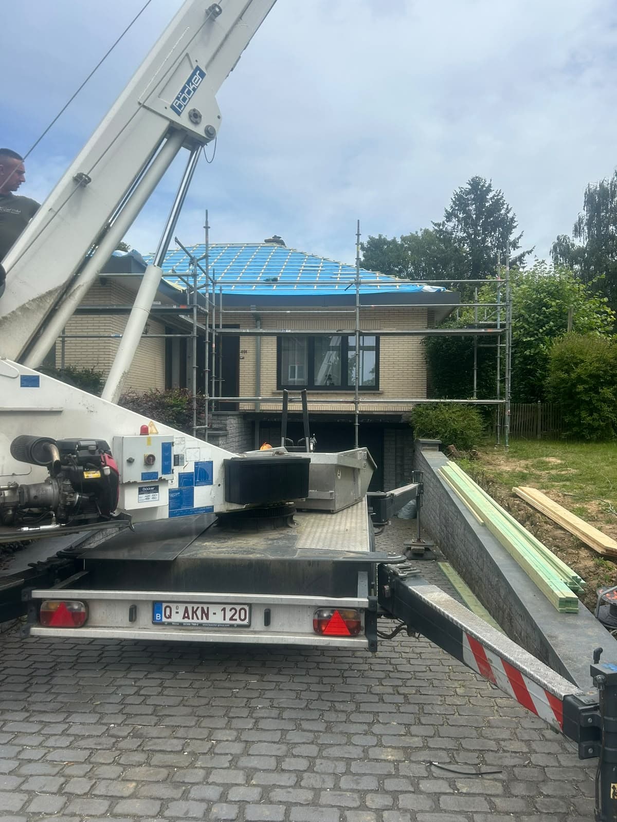 Camion-grue blanc stationné devant une maison avec échafaudages et toit en cours de rénovation bleue.